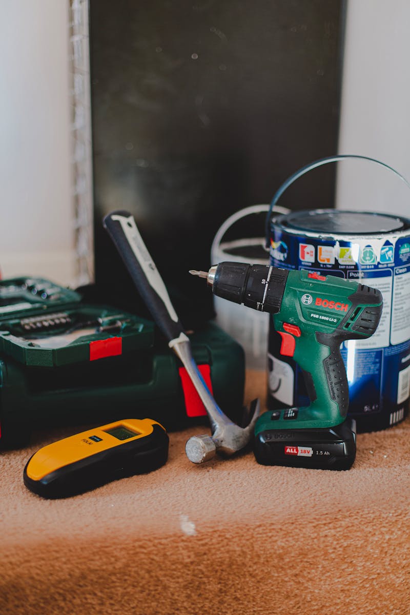 A selection of essential tools for home improvement projects, featuring a drill, hammer, and paint supplies.